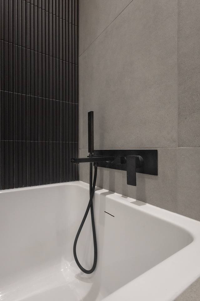 Baignoire et robinetterie noire devant une tuile cannelée