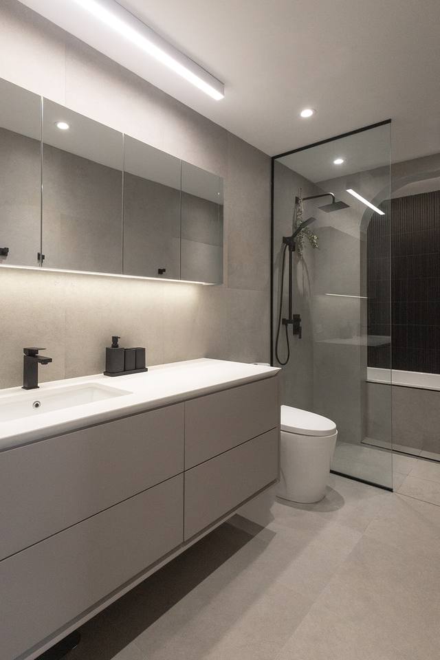 Salle de bain grise avec vanité, douche vitrée et éclairage intégré