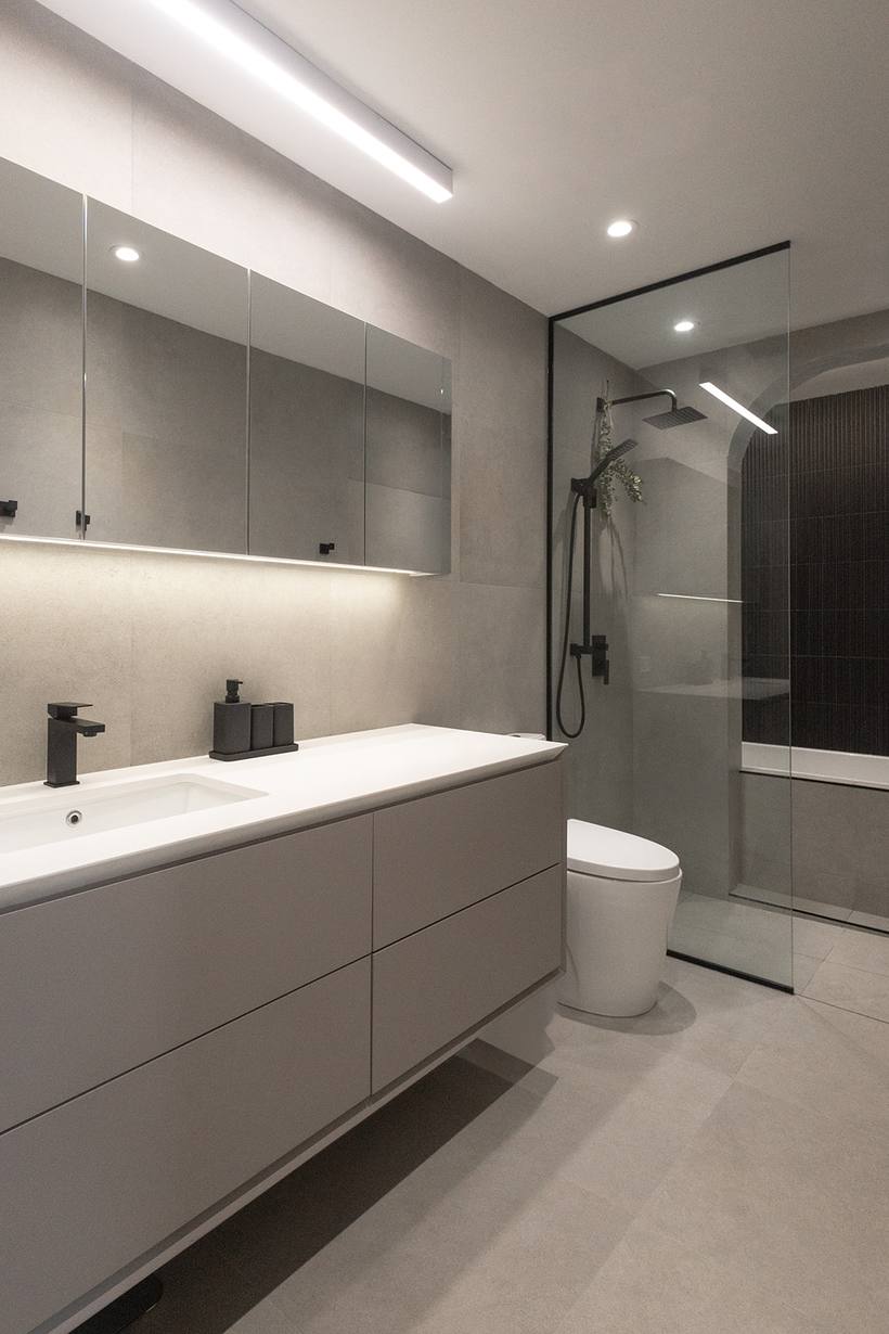 Salle de bain grise avec vanité, douche vitrée et éclairage intégré
