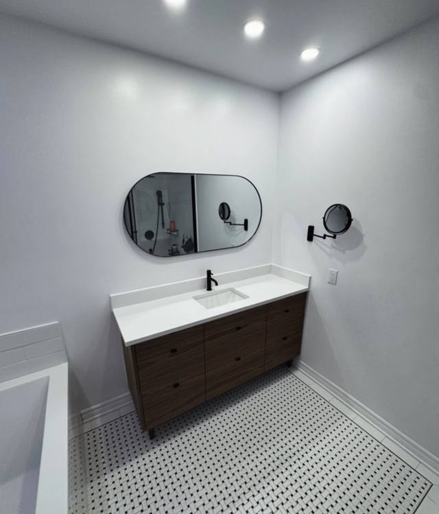Salle de bain avec miroir arrondi noir, vanité en bois foncé et plancher en mosaïque